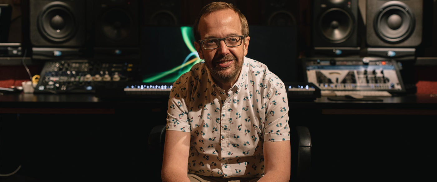 Steinway Artist and composer Kevin Kern wearing a short sleeve patterned shirt and glasses, seated, with recording studio equipment in background