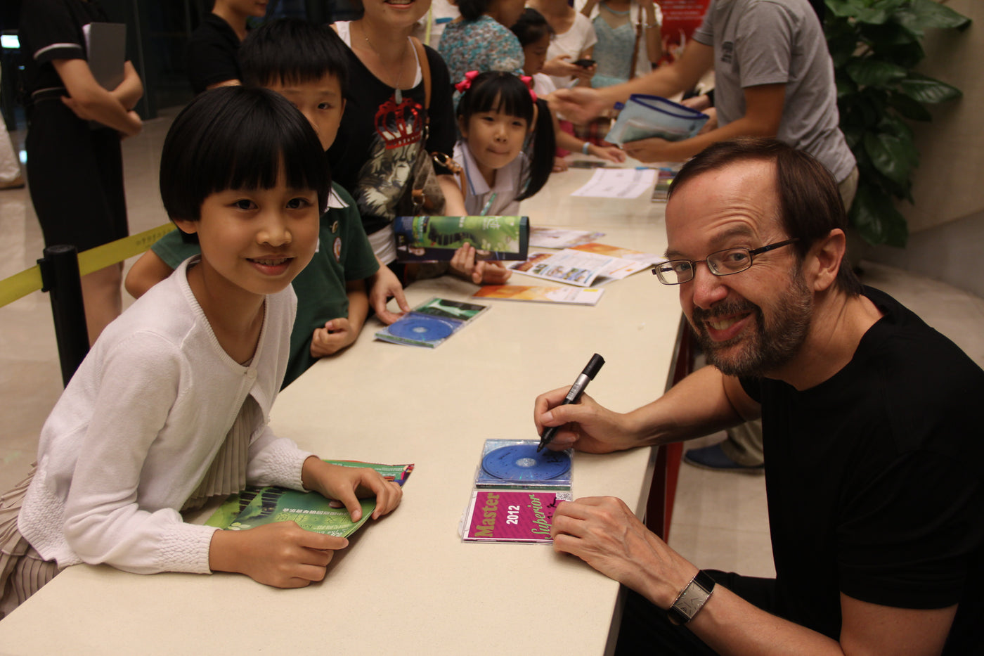 pianist Kevin Kern autographs a CD for a young girl with short dark hair wearing a white sweater while other young fans look on.